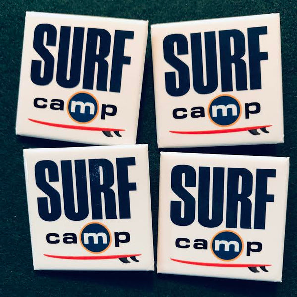A white square pin with words: SURF camp and a sideview of a surfboard.